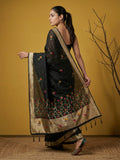 Woman wearing a black saree with floral patterns against a yellow wall.