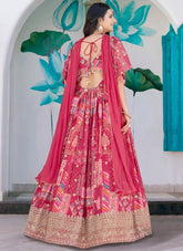 Woman in a pink traditional outfit with intricate patterns, standing against a decorative wall.