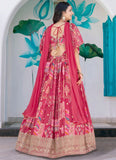 Woman in a pink traditional outfit with intricate patterns, standing against a decorative wall.