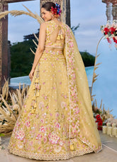 Woman in a yellow embroidered traditional outfit with floral decorations, standing outdoors.