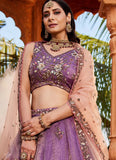 Woman wearing a traditional outfit with a purple blouse and pink dupatta in an outdoor setting.