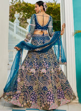 Woman in a traditional embroidered outfit with a blue dupatta standing in a decorative setting.