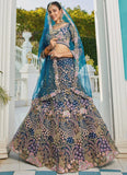 Woman in a traditional embroidered lehenga with a blue dupatta standing outdoors.