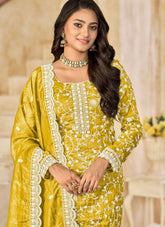 Woman wearing a yellow traditional outfit with white embroidery in an indoor setting.