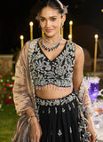 Woman in traditional black and silver embroidered outfit with jewelry, standing outdoors at night.