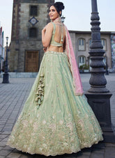 Woman in a light green embroidered lehenga with pink dupatta standing on a street.