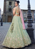 Woman in a light green embroidered lehenga with pink dupatta standing on a street.