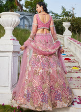 Woman in a pink and gold traditional outfit standing on a decorative staircase with floral arrangements.