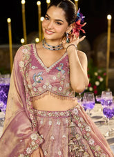 Woman in traditional pink embroidered outfit with floral decorations, standing in a decorated indoor setting.