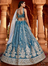 Woman in a blue embroidered traditional outfit standing in front of ornate columns.