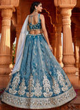 Woman in a blue embroidered traditional outfit standing in front of ornate columns.