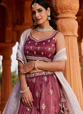 Woman in traditional maroon and white outfit with jewelry against an architectural background