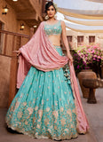 Woman in a traditional outfit with a pink dupatta and turquoise lehenga in an outdoor setting.
