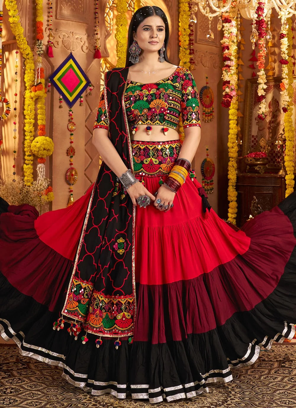 Woman in a traditional red and black embroidered outfit with colorful jewelry against a decorated background.