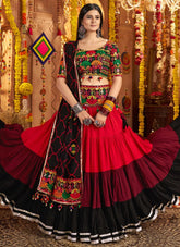 Woman in a traditional red and black embroidered outfit with colorful jewelry against a decorated background.