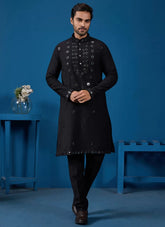 Man wearing a black sherwani with intricate designs against a blue background