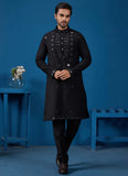 Man wearing a black sherwani with intricate designs against a blue background