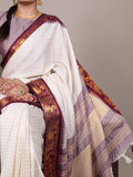 White saree with purple and gold border worn by a person on a gray background