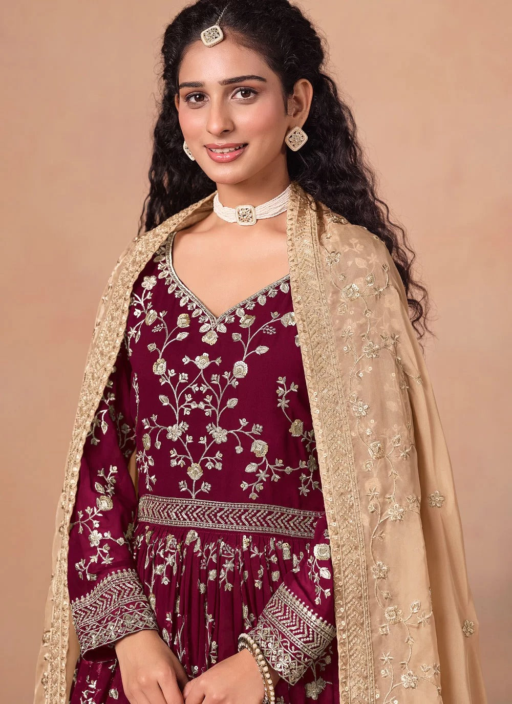 Woman wearing a maroon embroidered outfit with a beige dupatta against a beige background