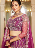 Woman in a traditional purple and pink embroidered outfit with jewelry in an ornate setting.