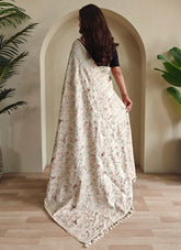 Woman wearing a floral saree standing in a room with plants.