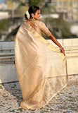 Woman in a beige saree standing outdoors with blurred background
