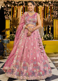 Woman in a pink embroidered traditional outfit standing in a decorated indoor setting.