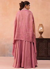 Woman in a pink traditional outfit standing against a peach-colored wall with a lamp and wooden cabinet.