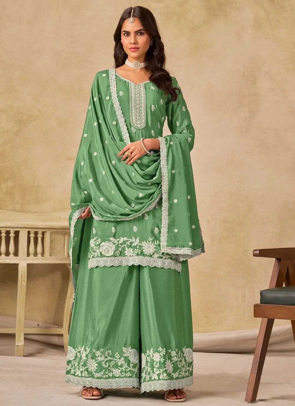 Woman wearing a green traditional outfit with white embroidery against a beige background