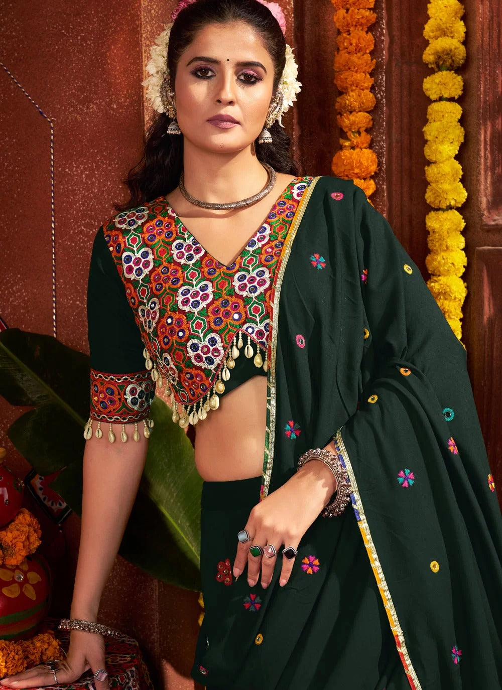 Woman in traditional dark green saree with colorful blouse against a decorative background