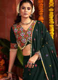 Woman in traditional dark green saree with colorful blouse against a decorative background