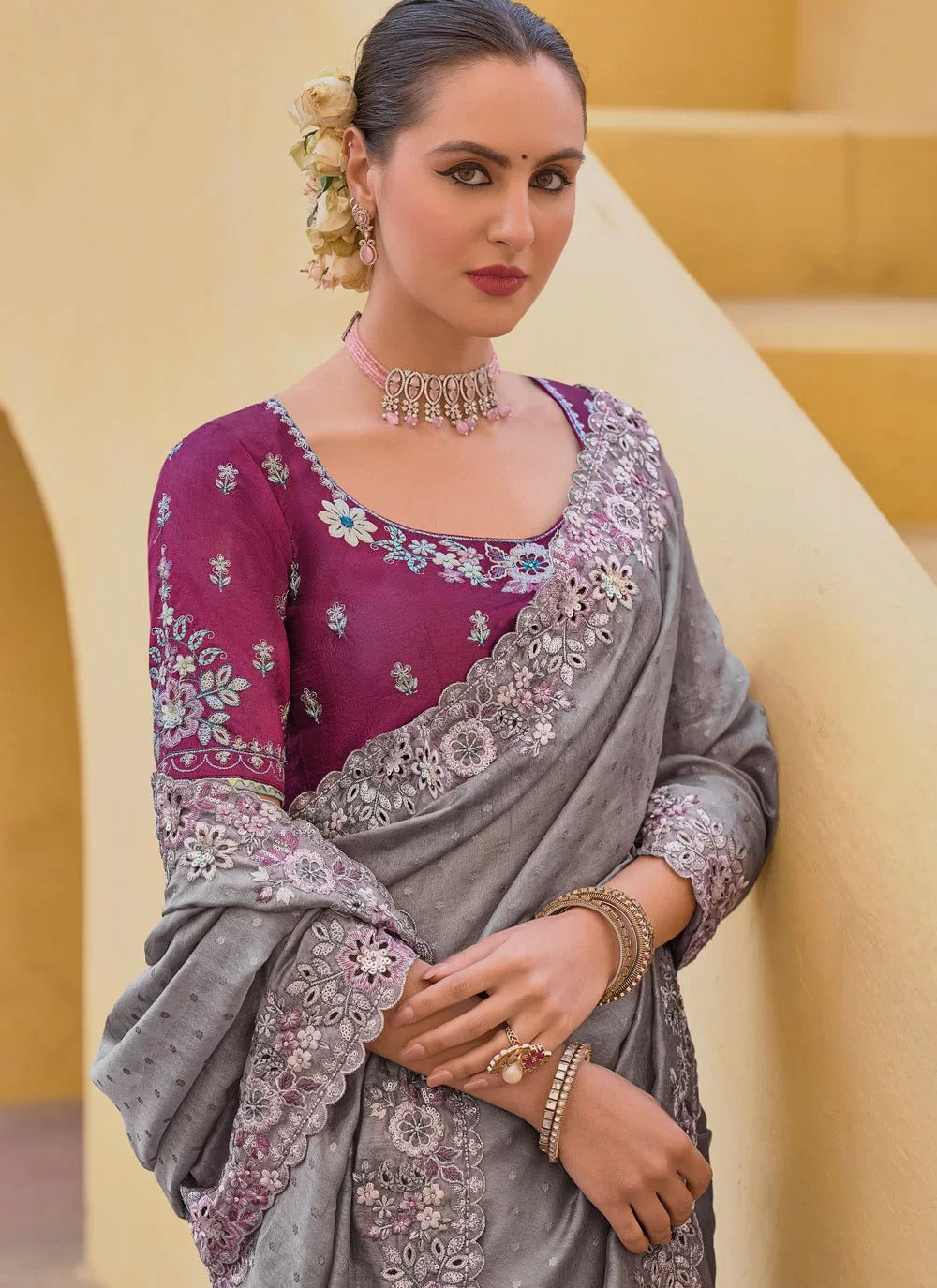 Woman wearing a traditional outfit with a purple blouse and gray saree against a beige background