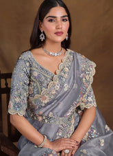 Woman wearing a gray saree with floral embroidery against a brown background