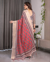 Woman wearing a red and beige saree with a pattern, standing indoors.