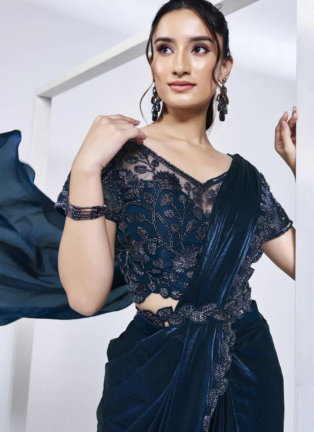 Woman wearing a dark blue saree with lace detailing against a white background