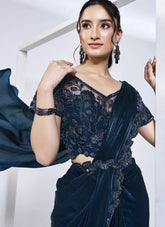 Woman wearing a dark blue saree with lace detailing against a white background