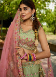 Woman in traditional green and pink embroidered outfit with jewelry, standing outdoors.