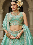 Woman in traditional green embroidered outfit with jewelry against a stone archway background