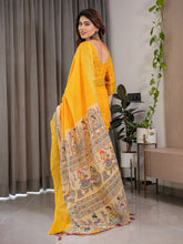 Woman wearing a yellow saree with intricate patterns indoors.