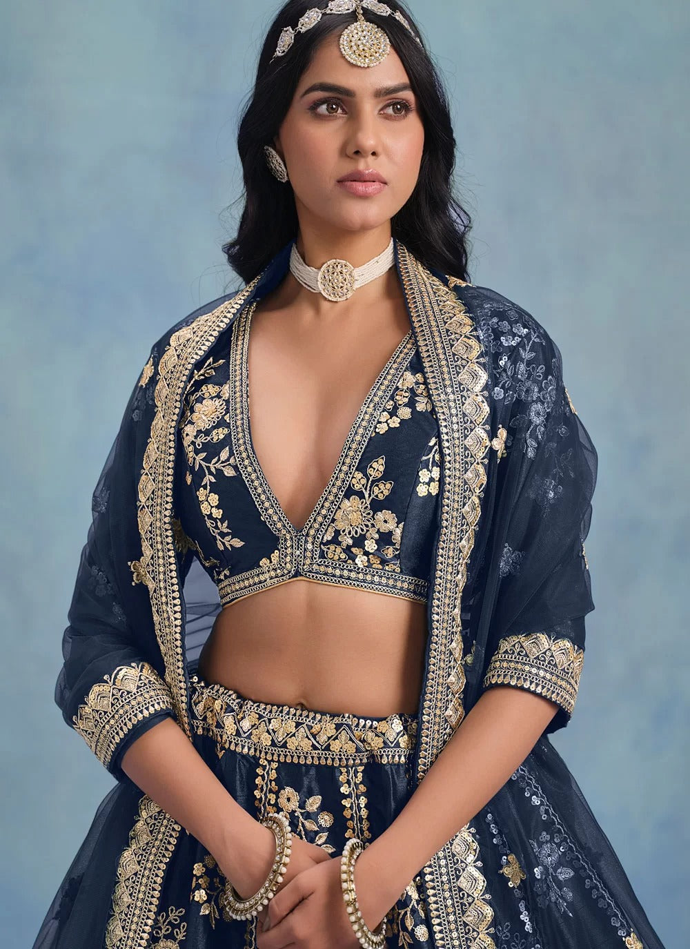 Woman wearing a traditional navy blue embroidered outfit with gold details against a light blue background