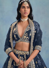 Woman wearing a traditional navy blue embroidered outfit with gold details against a light blue background