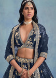 Woman wearing a traditional navy blue embroidered outfit with gold details against a light blue background