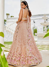 Woman in a pink embroidered lehenga standing outdoors with a fountain in the background