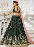 Woman in a dark green embroidered lehenga with a pink dupatta standing on a staircase.