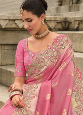 Woman wearing a pink saree with intricate embroidery sitting on steps.