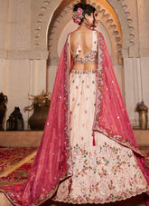 Woman in a traditional embroidered outfit with a pink dupatta standing in front of an archway.