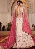 Woman in a traditional embroidered outfit with a pink dupatta standing in front of an archway.