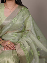 Light green saree with intricate patterns held by a person against a neutral background