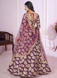 Woman wearing a purple and gold traditional outfit with a sheer dupatta in a room.