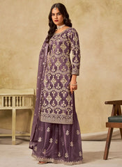 Woman wearing a purple embroidered traditional outfit against a beige wall.